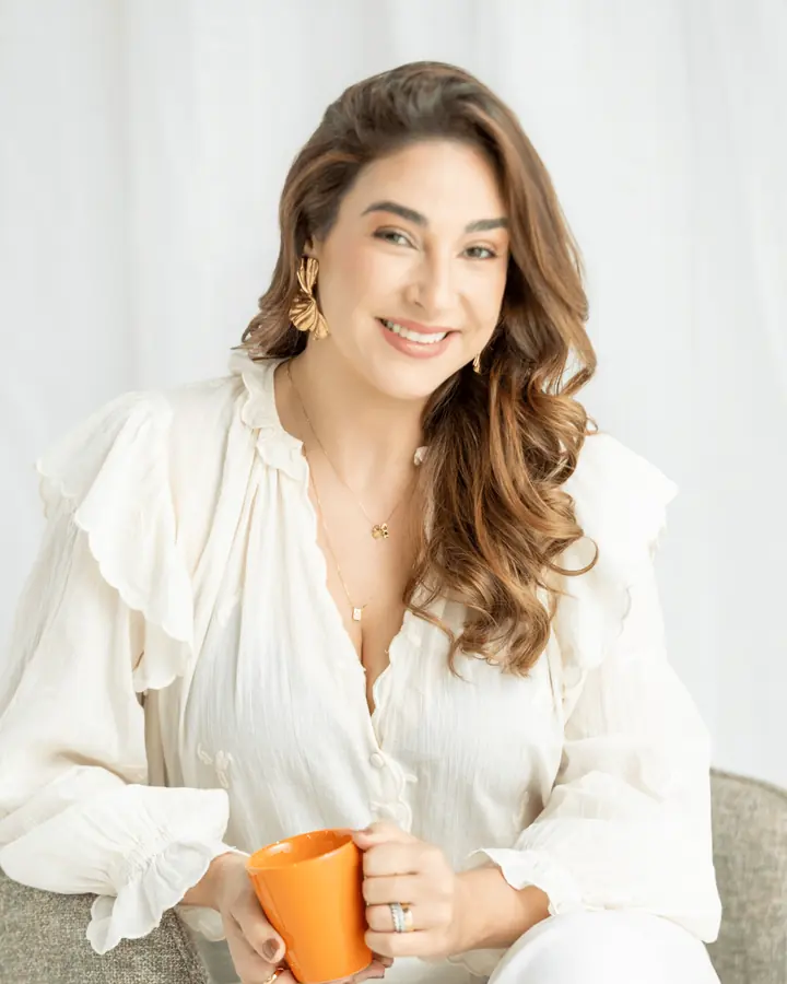 Nutricionista Luciana Medeiros sorrindo, de blusa branca, segurando uma caneca