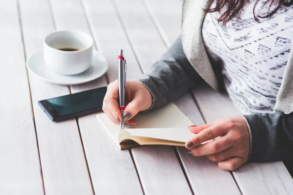 Mulher anota o que comeu em um caderno na cozinha, ao lado de cuscuz com ovo, café, exames impressos e caixa de remédios