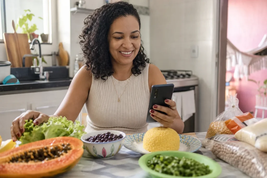 Mulher em cozinha de casa separando alimentos e rótulos para consulta nutricionista online.
